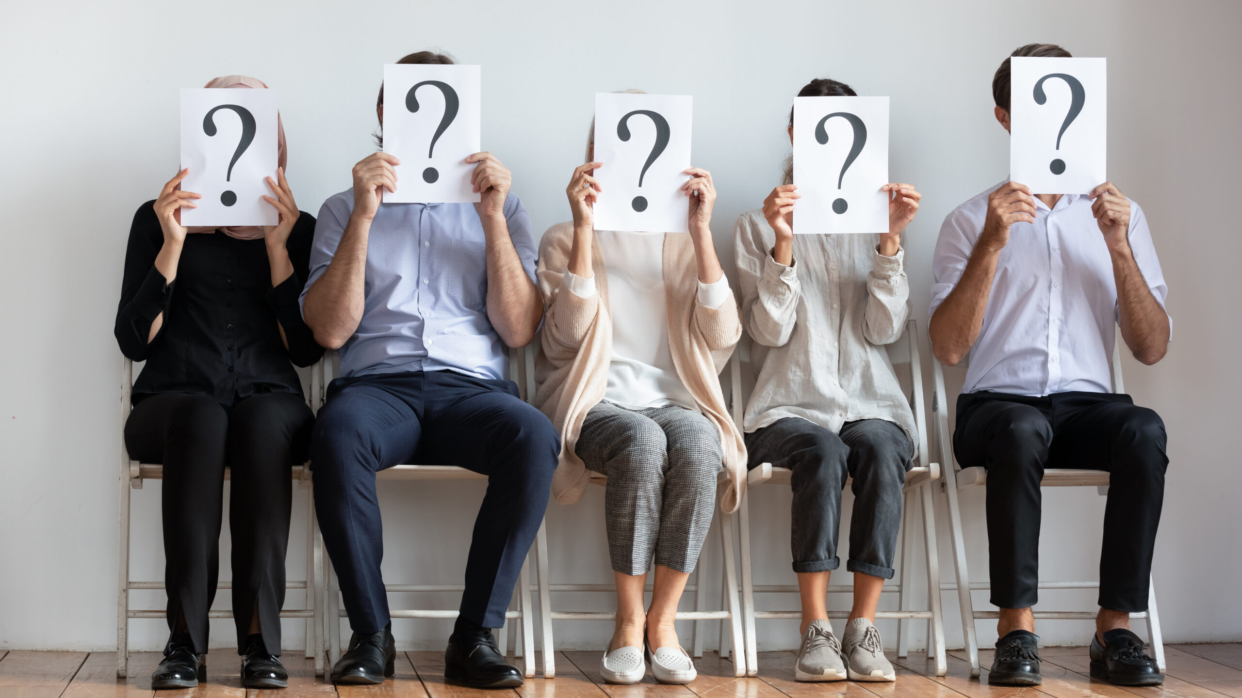 Unconscious bias in recruitment - five candidates sit in a waiting room on chairs. Their identities are hidden behind large signs with question mark symbols on.