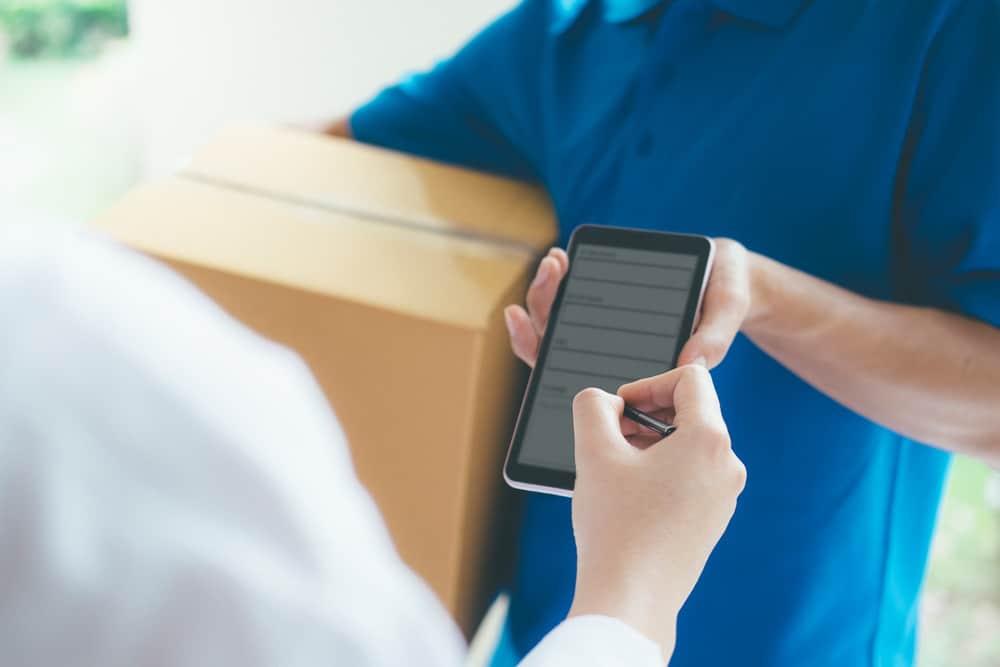 Employment Status - A courier delivers a parcel and presents a woman with a tracking device for a signature - Gig economy worker