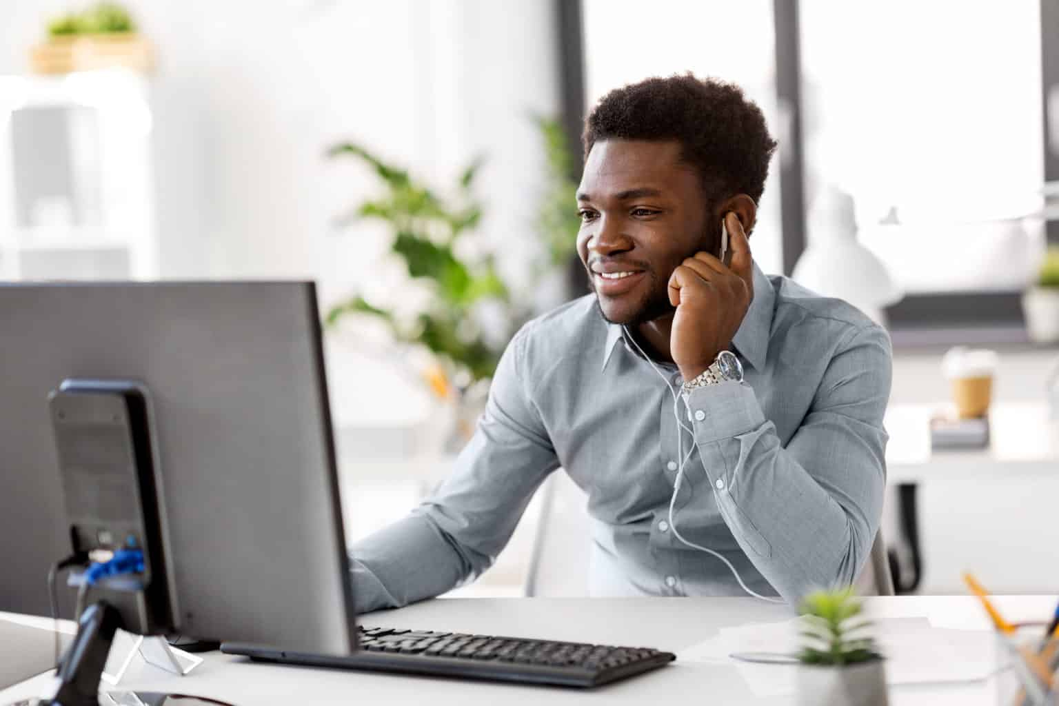 Hybrid working: return t o the office after coronavirus. Man sits at desk in front of a computer monitor, wearing earphones on a team video meeting