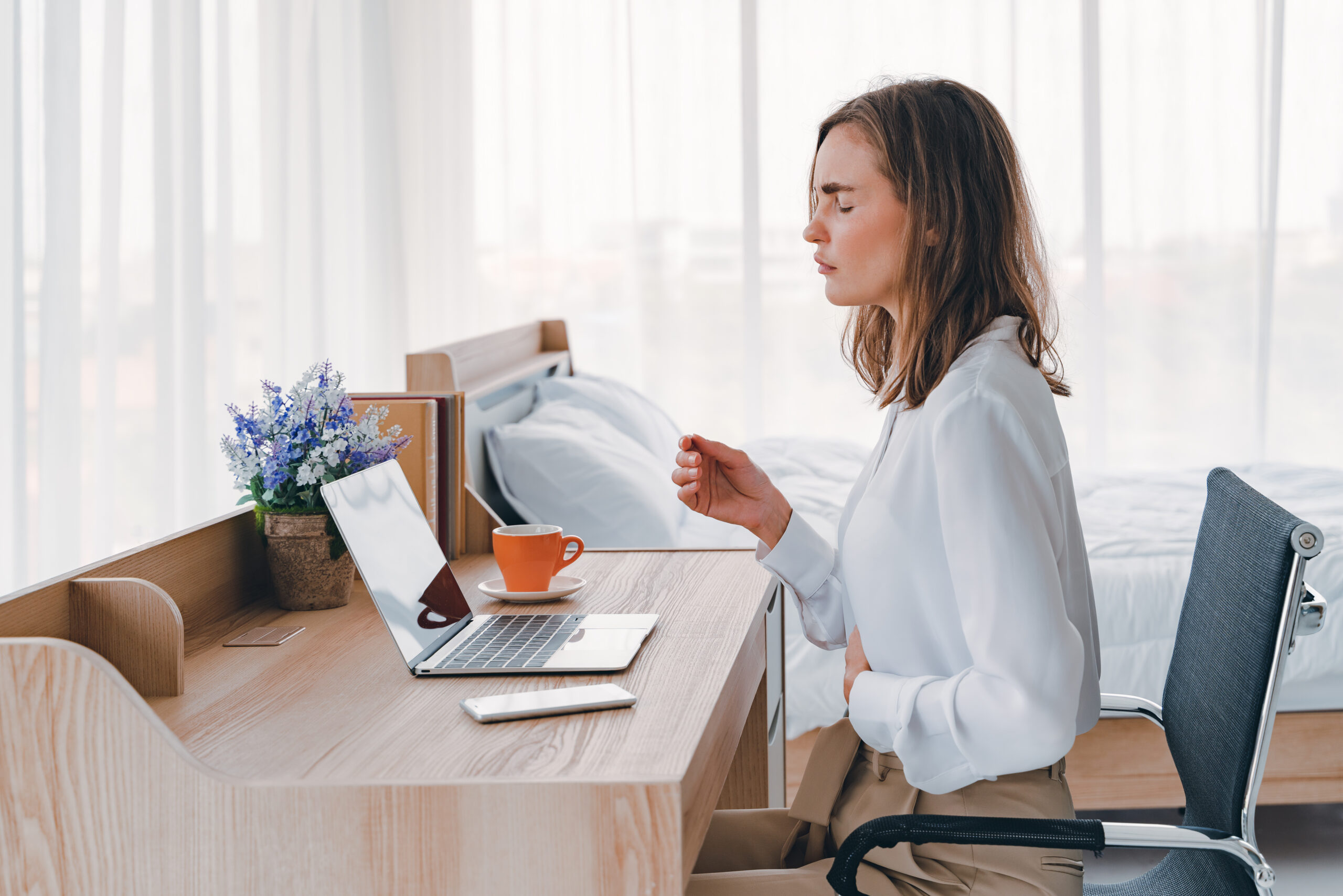 a woman sitting at a desk with a laptop and a cup of coffee. Endometriosis in the workplace.